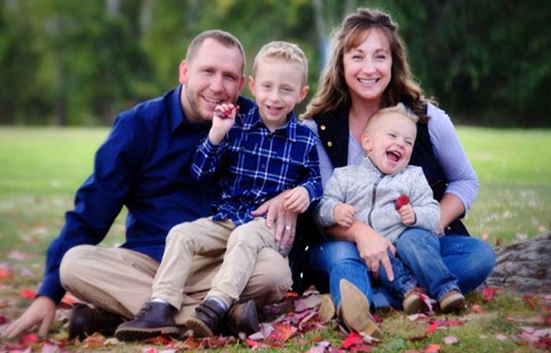 A young family of four sits under a tree in the grass