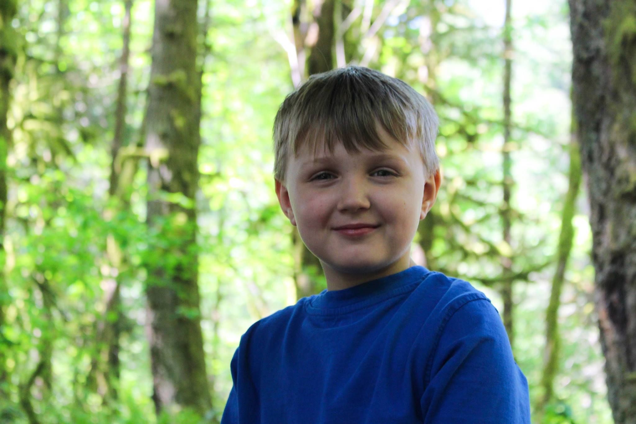 Boy stands in forest of trees smiling