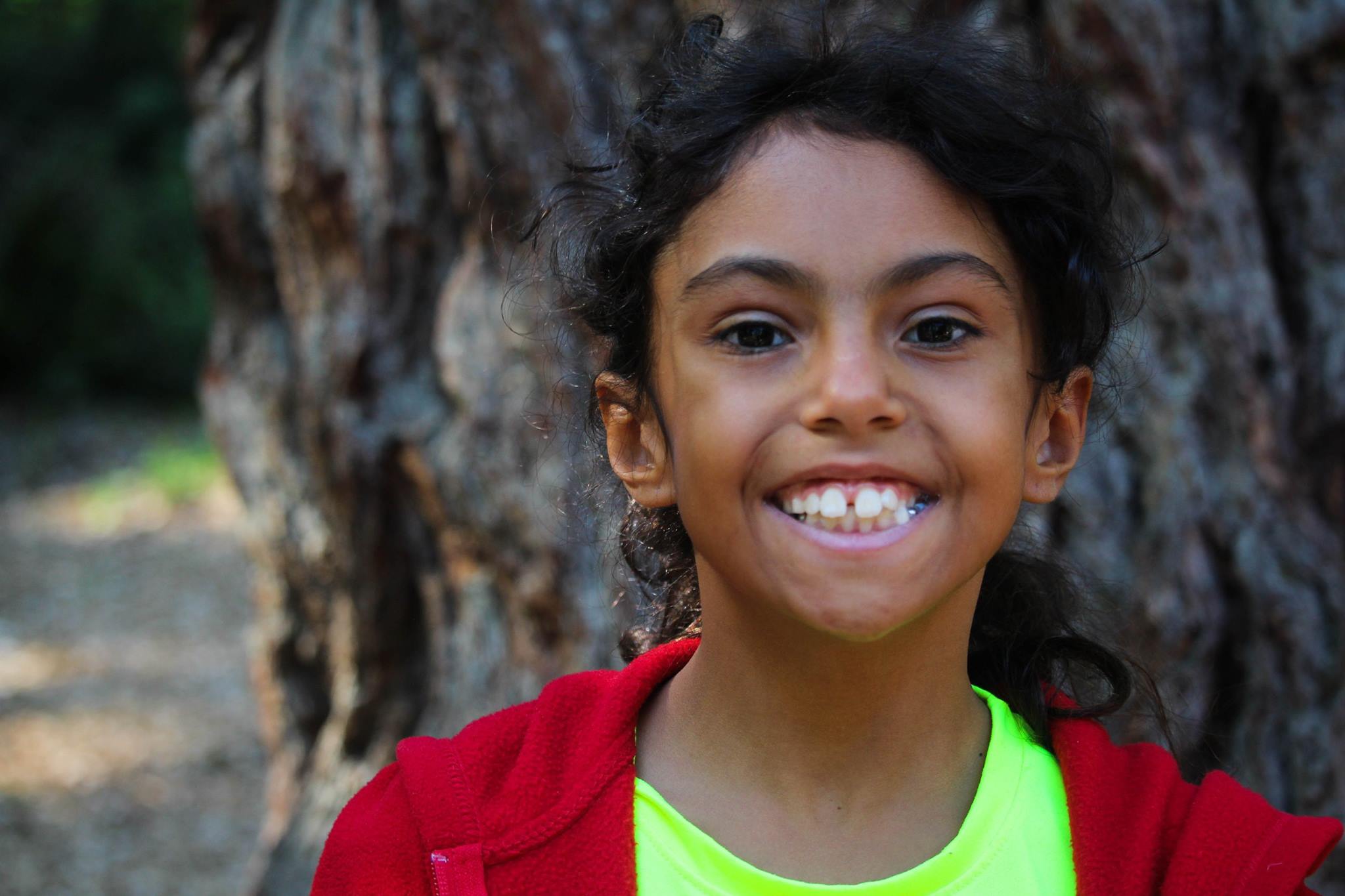 Young smiling girl stands by tree
