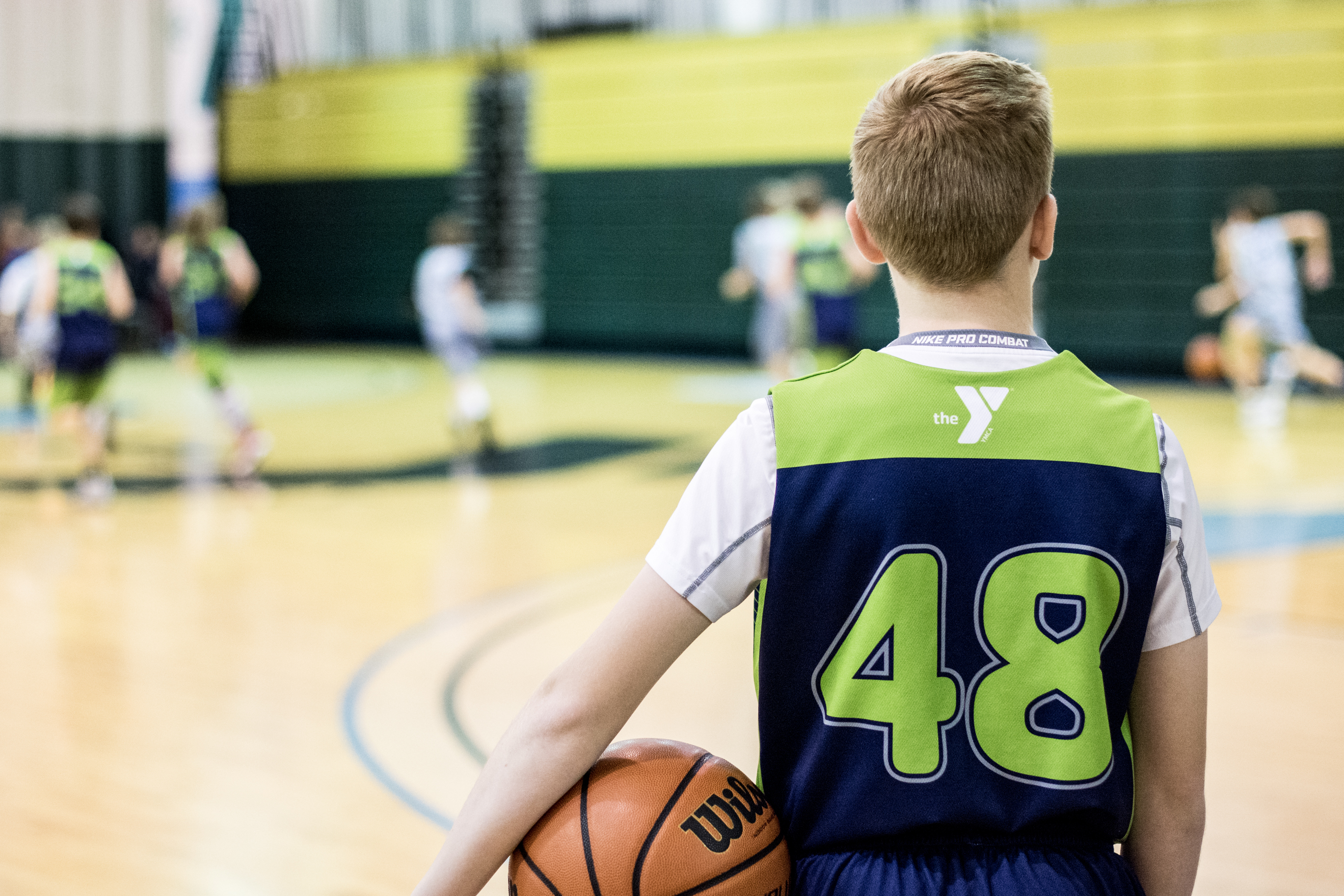 Boy holds basketball, while looking out over gym court