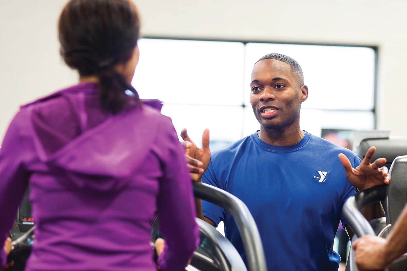 Personal trainer assists member on treadmills
