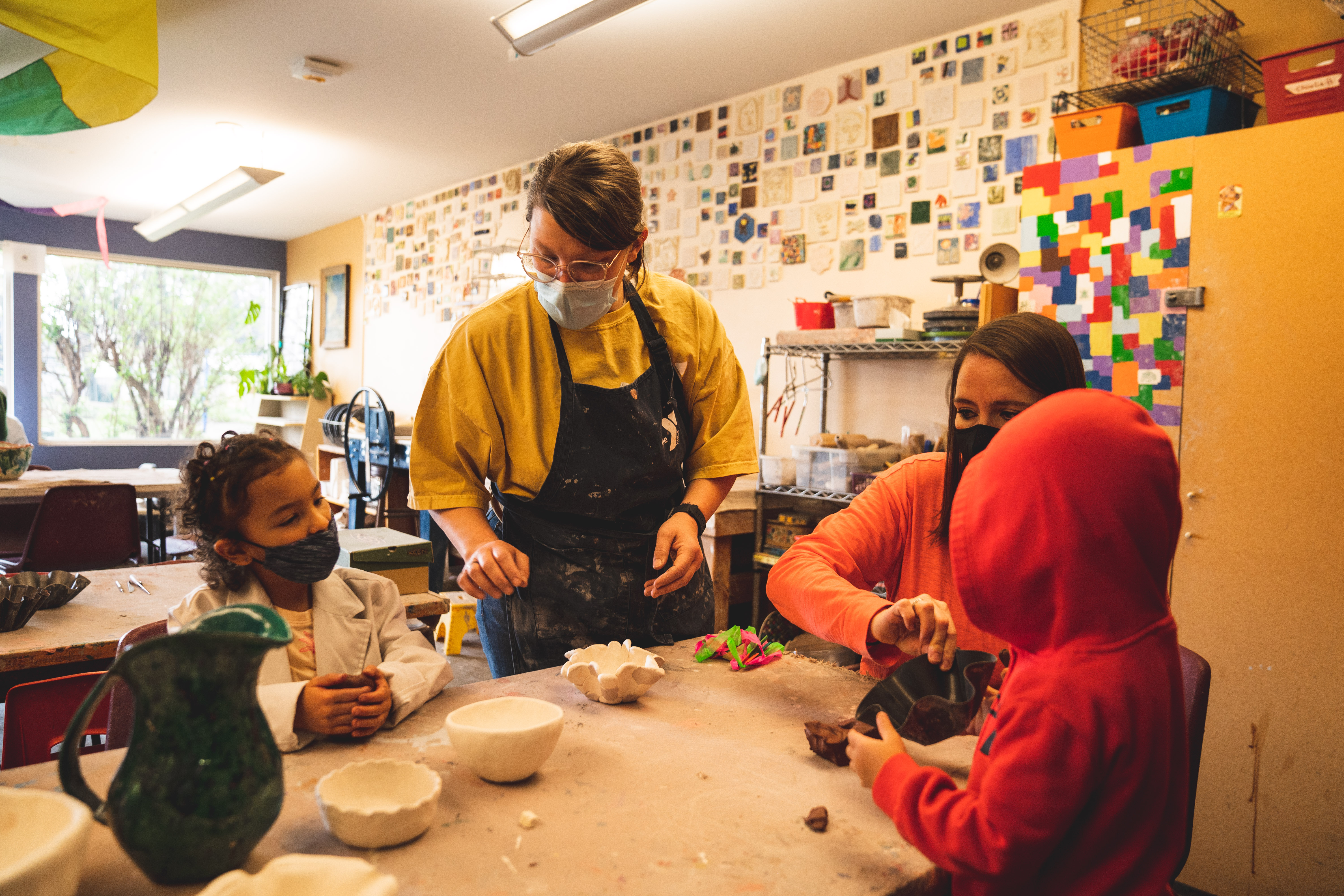 two adults helping two children make clay pinch pots
