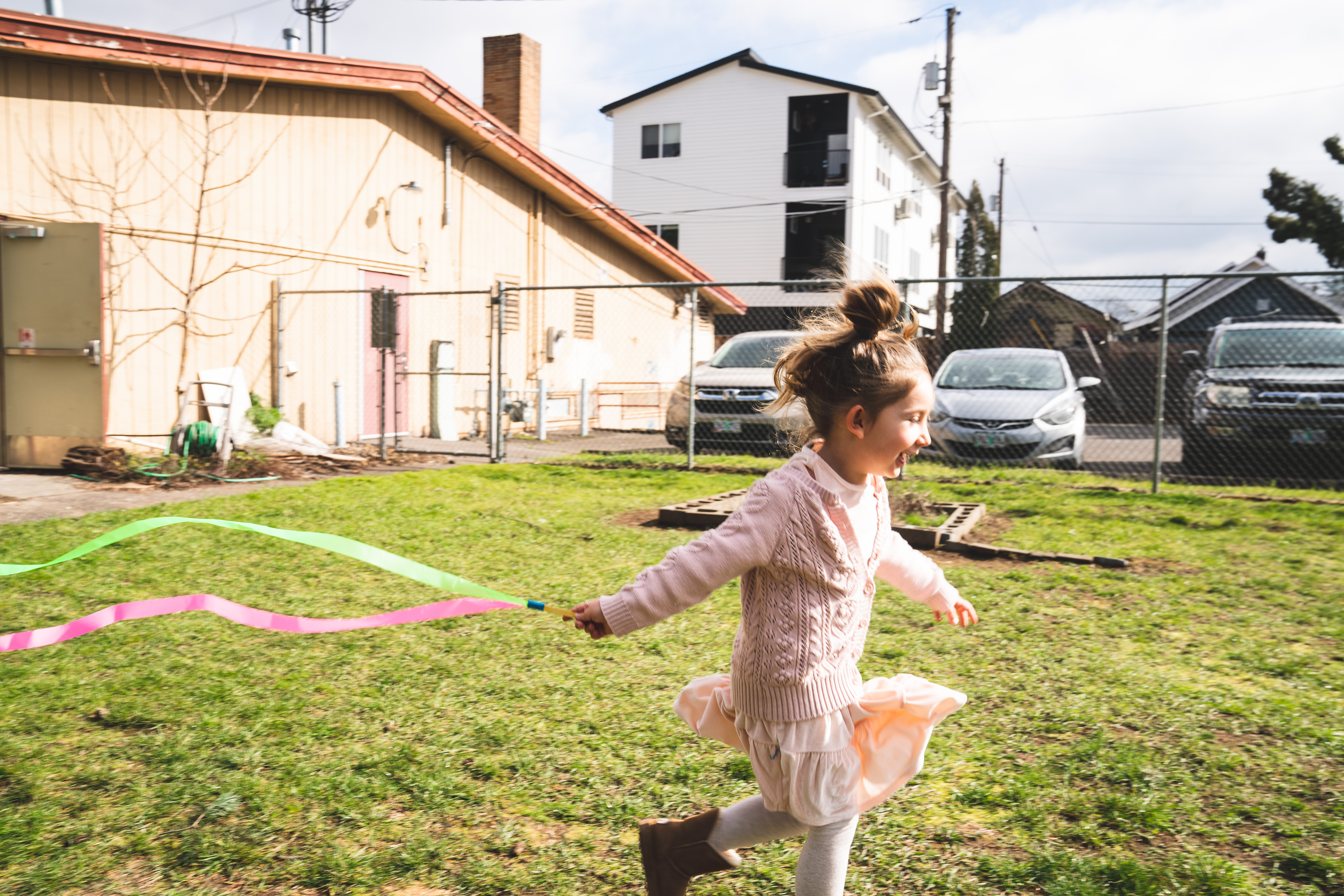 A little girl runs through a grass field with a ribbon wand behind her